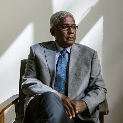 An Elderly Man in Gray Suit Sitting on a Wooden Armchair